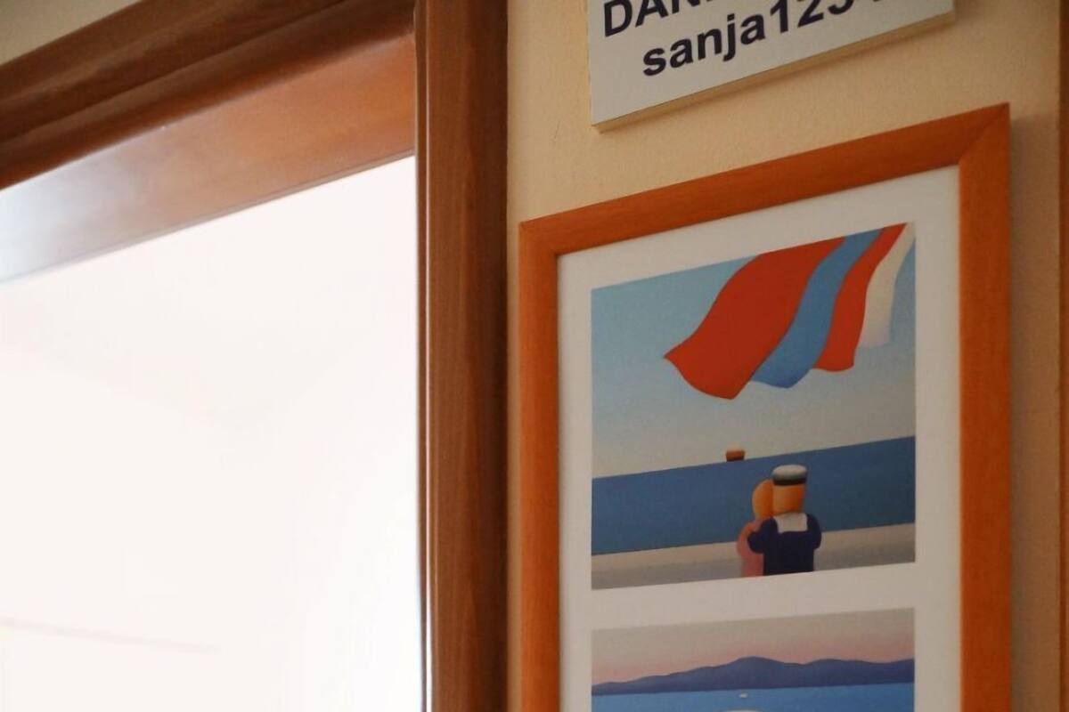 A framed artwork on a wall, a bed with a red bedspread, and a sign with text.