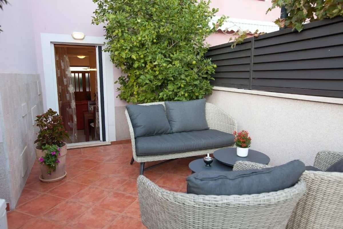 Une terrasse avec des meubles en osier, une plante en pot et une petite table.