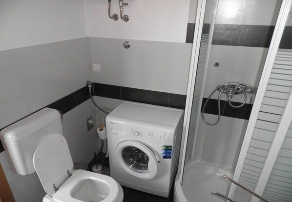 A compact bathroom with a toilet, washing machine, and shower. - Apartments Sora (Preko)