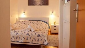 Een slaapkamer met een houten plafond, een bed met beddengoed met een patroon, bedlampen, een nachtkastje, een dressoir en een lijst met daarin een afbeelding van een maan boven water aan de muur.