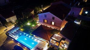 Luchtbeeld van een woonhuis met zwembad, overdekt terras en een goed verlicht huis.