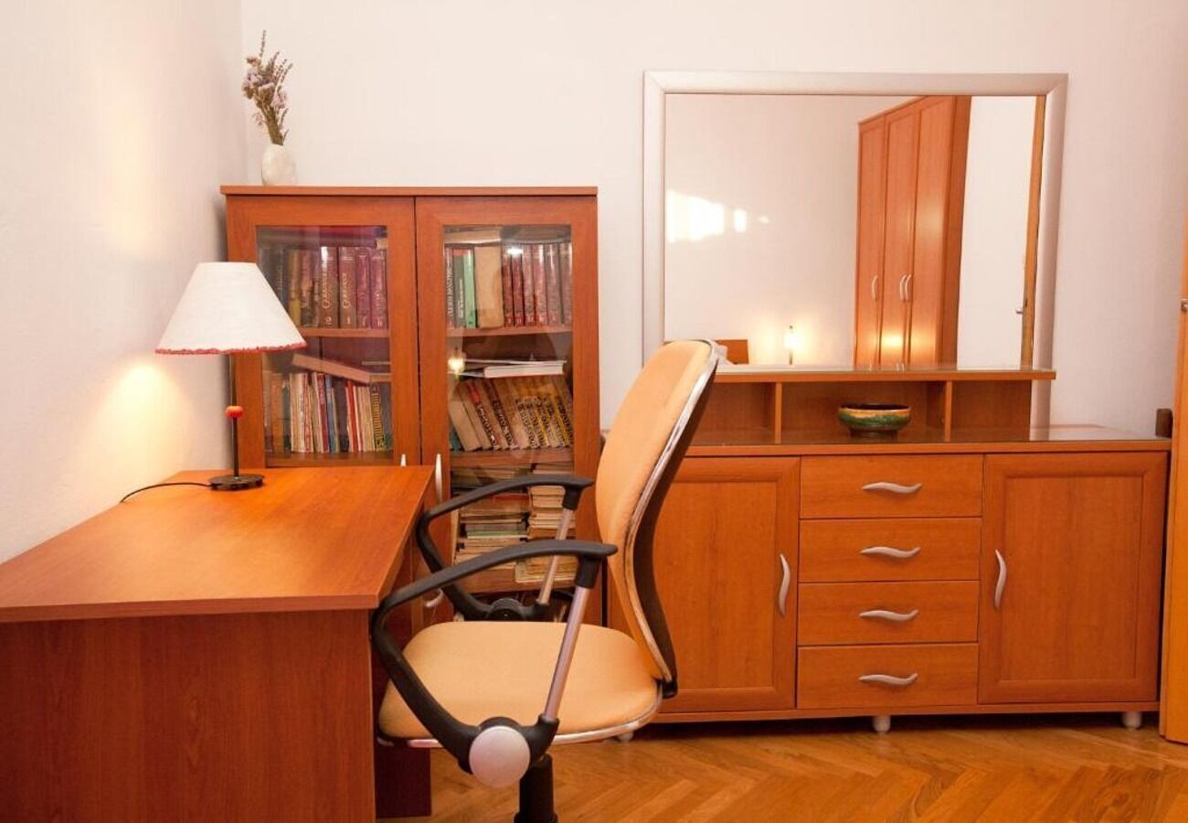 A room with a wooden desk, a chair, a bookshelf, a cabinet, and a mirror.