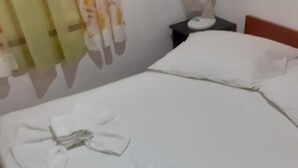 A neatly made bed with towels folded into bows, a bedside table with a lamp, and a wall with curtains. - House Senka1 (Vela Luka)
