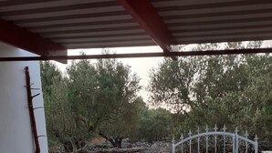 An outdoor patio area with a stone barbecue station, a metal gate, and a view of trees and rocks. - House Senka1 (Vela Luka)