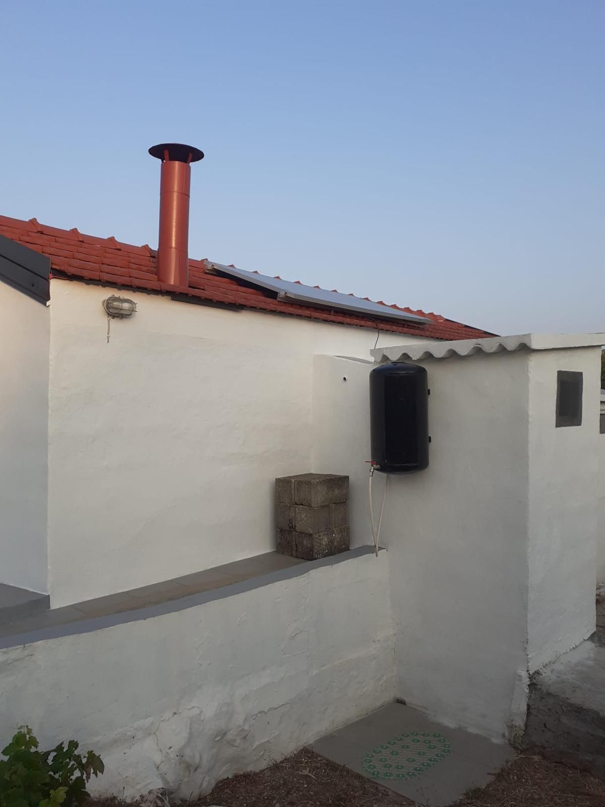 Un bâtiment avec un toit recouvert de tuiles rouges, une cheminée et un réservoir d’eau.