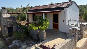 A small, single-story house with a stone fireplace, a red-tiled roof, and a garden with various plants and flowers. - House Senka1 (Vela Luka)
