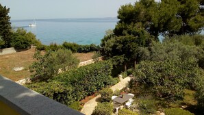 A view of a garden with a stone pathway, a table with chairs, and a sailboat on the water. - Apartment Brane (Preko)