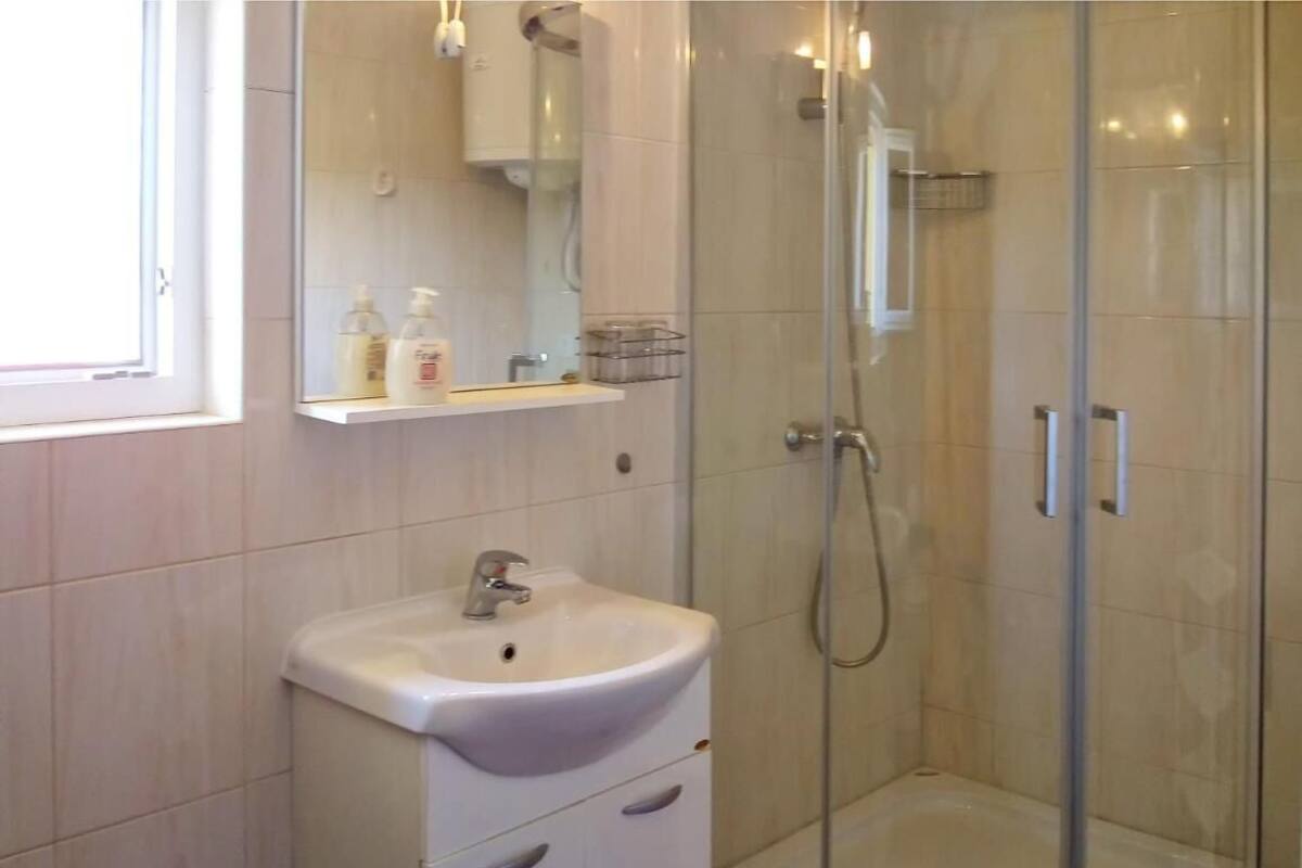Une salle de bain avec un lavabo blanc, une cabine de douche en verre et un miroir au-dessus du lavabo.