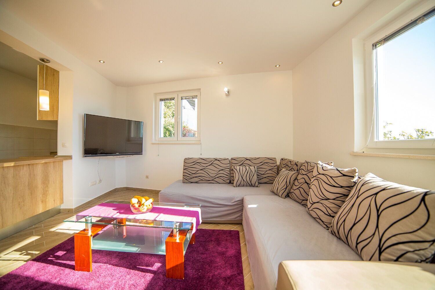 Een moderne woonkamer met een bank, een glazen salontafel, een flatscreen-tv en een raam met uitzicht op groen.