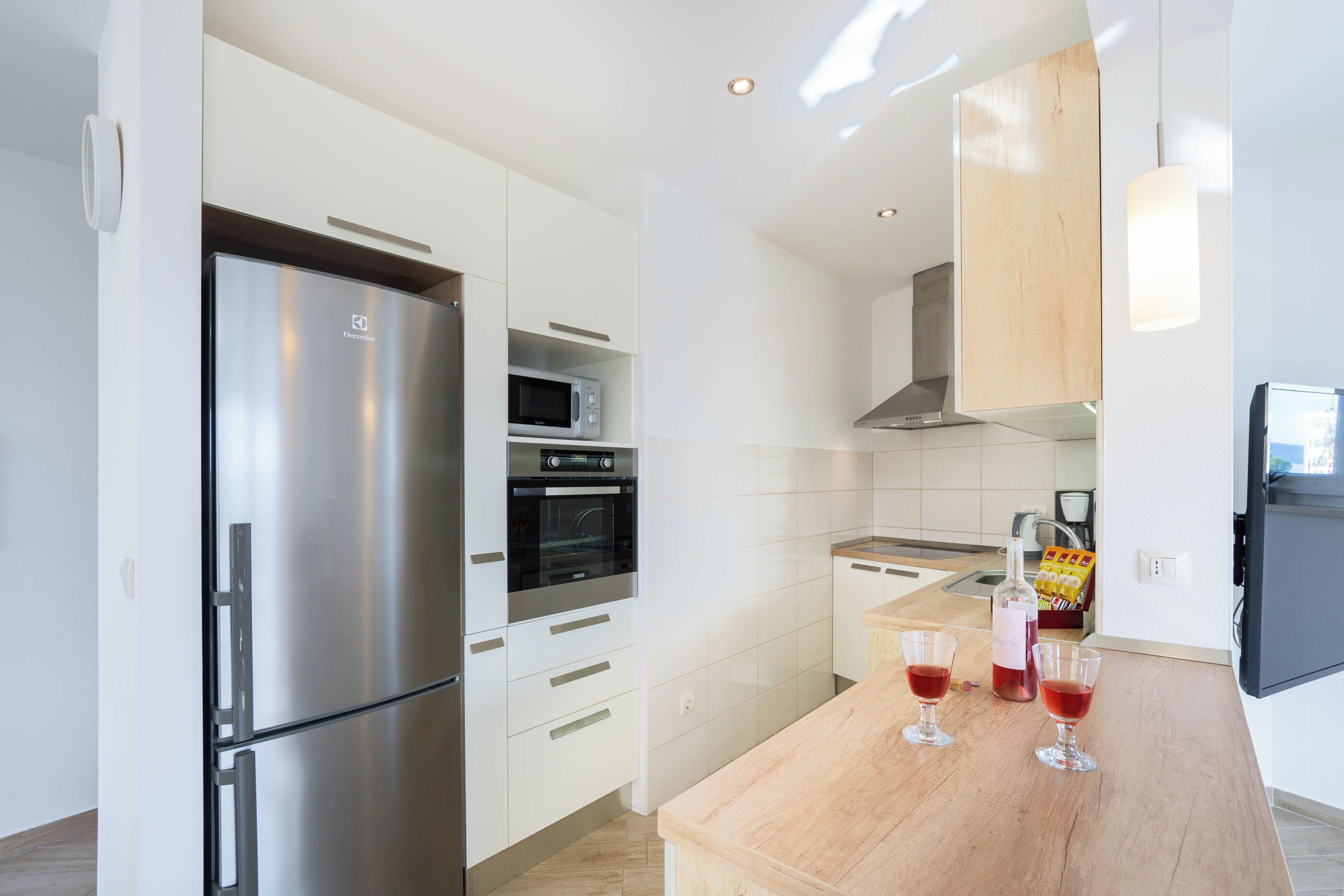 A modern kitchen with stainless steel appliances, white cabinetry, and a wooden countertop.