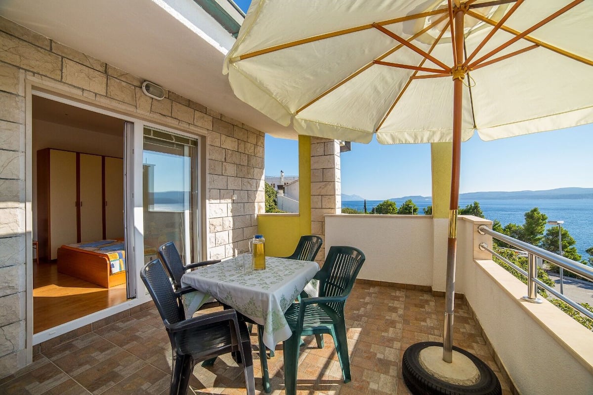 A balcony with a table and chairs, a white umbrella, and a view of the sea.