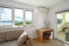 Ein Zimmer mit Schreibtisch, Stuhl und einer Couch, mit Blick ins Freie.