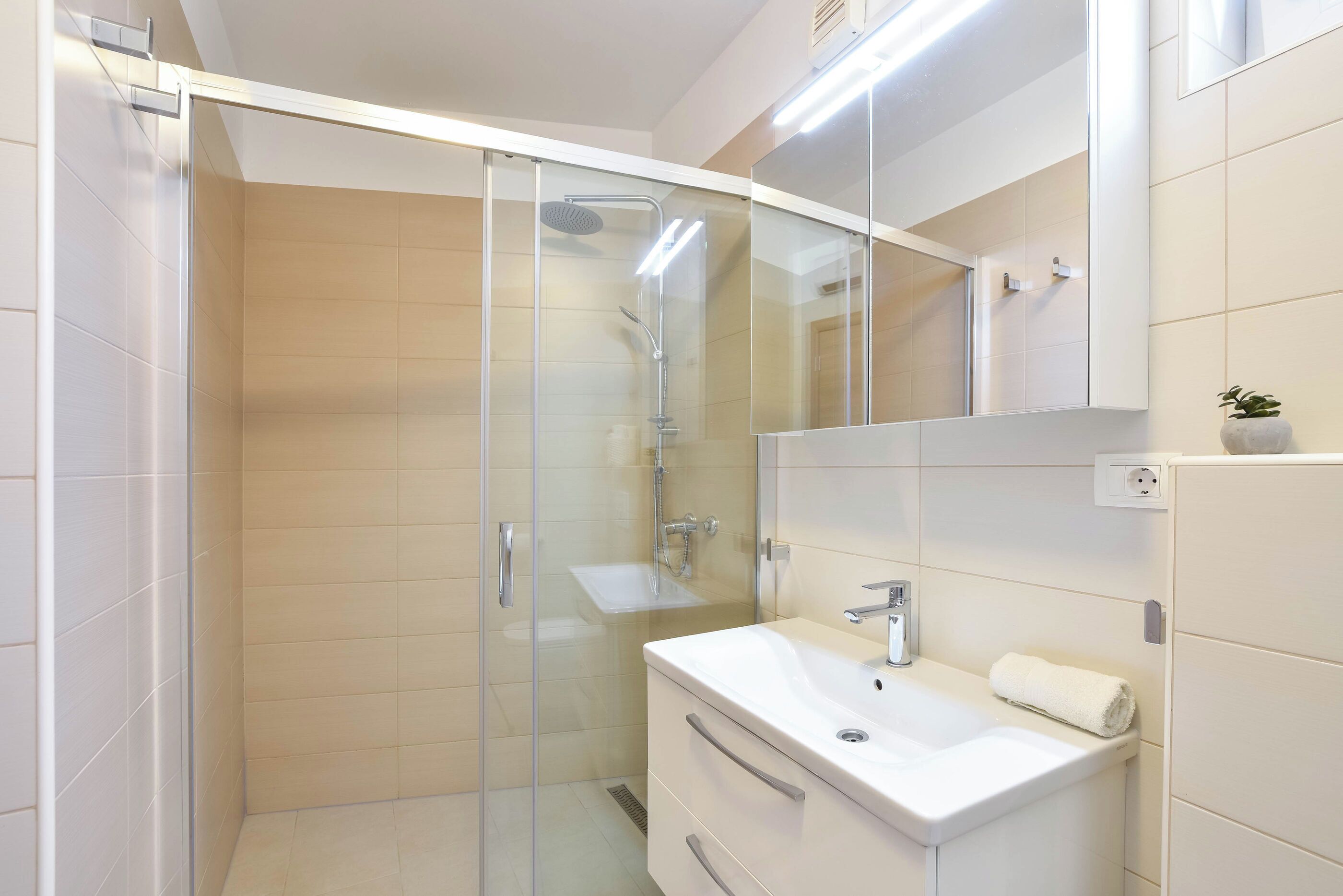Un baño moderno con ducha envuelta en vidrio, un lavabo blanco y un espejo sobre la consola.