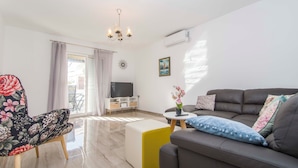 A modern living room with a sofa, a floral armchair, a TV, and a small table with a vase of flowers. - House Branka (Vir)