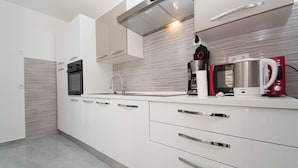 A modern kitchen with white cabinets, stainless steel appliances, and a sleek backsplash. - House Branka (Vir)