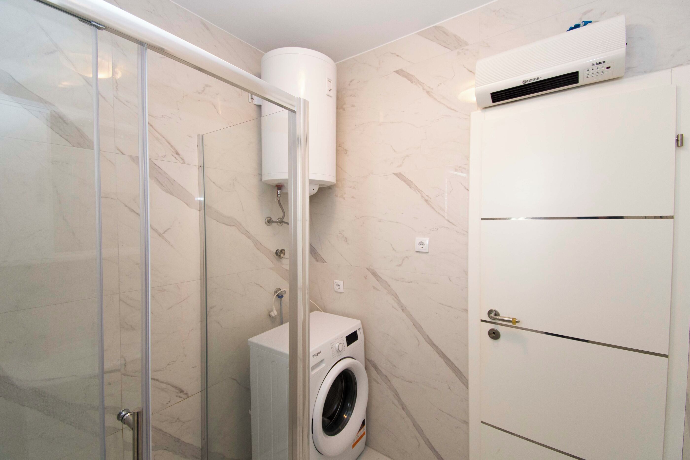 A bathroom with a glass shower enclosure, a white washing machine, and a white cabinet.
