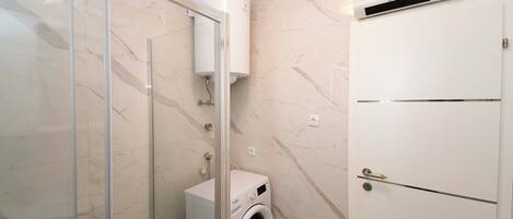 A bathroom with a glass shower enclosure, a white washing machine, and a white cabinet.