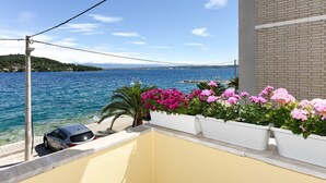 Ein Balkon mit Blick auf das Meer, ein geparktes Auto und Kübelblumen.
