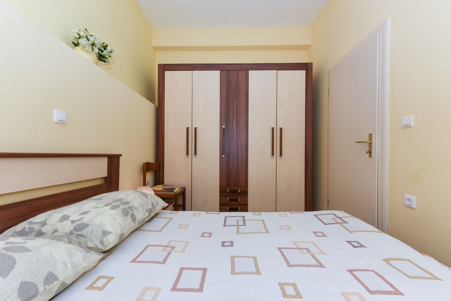 Un dormitorio con una cama, un armario de madera, una silla y una mesita.
