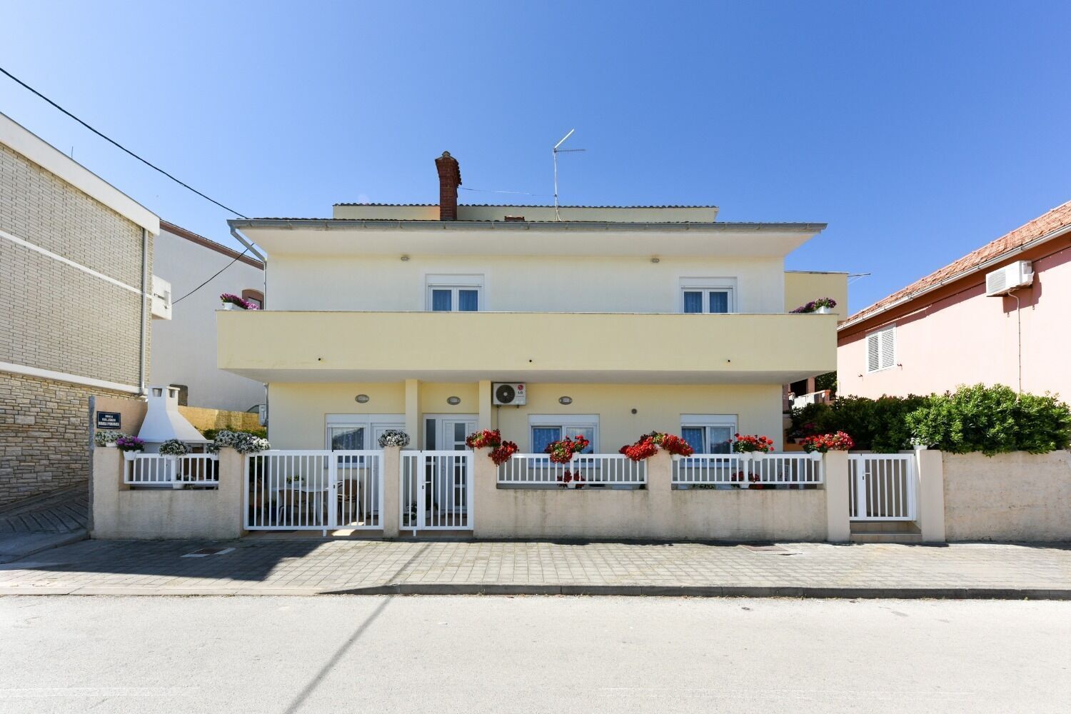 A two-story building with a flat roof, a chimney, and a balcony with flower boxes.