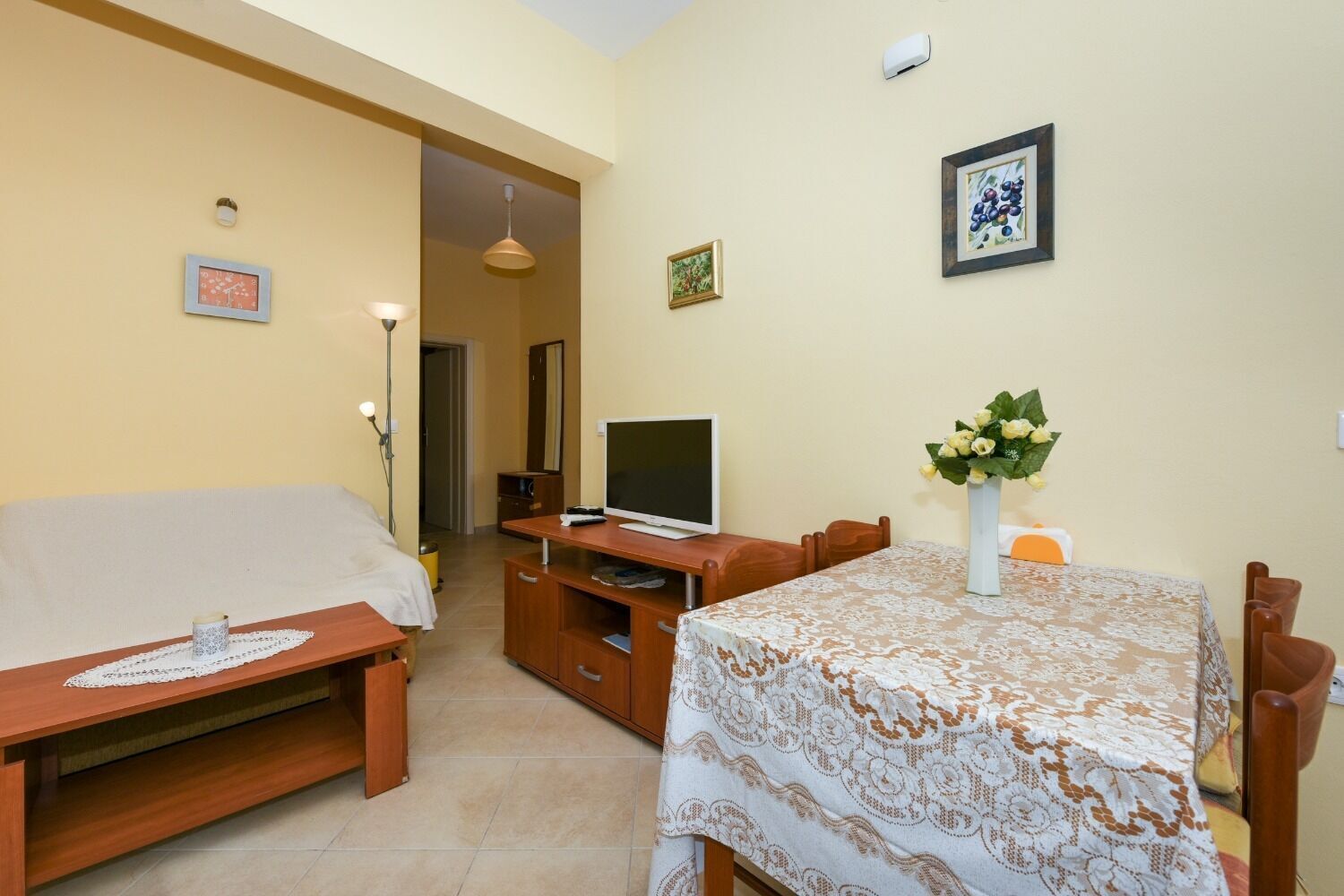 Una camera d'albergo con un letto, una televisione, un tavolo da pranzo con sedie, una piccola scrivania e un vaso di fiori.