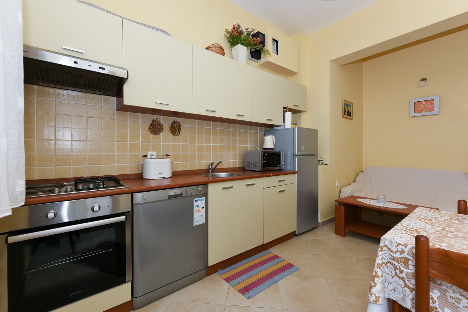 Una cucina funzionale con fornelli, forno, lavastoviglie, microonde e frigorifero. È presente un piccolo angolo ristoro con tavolo e sedie.
