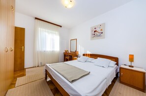 A hotel room with a bed, bedside table, chair, desk, and a painting on the wall. - Apartments Cloe (Zadar)