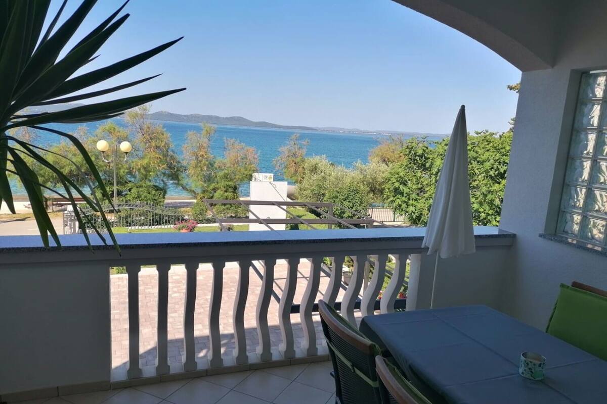 Un balcon avec vue sur la mer et les collines, une table avec une chaise et une plante en pot.
