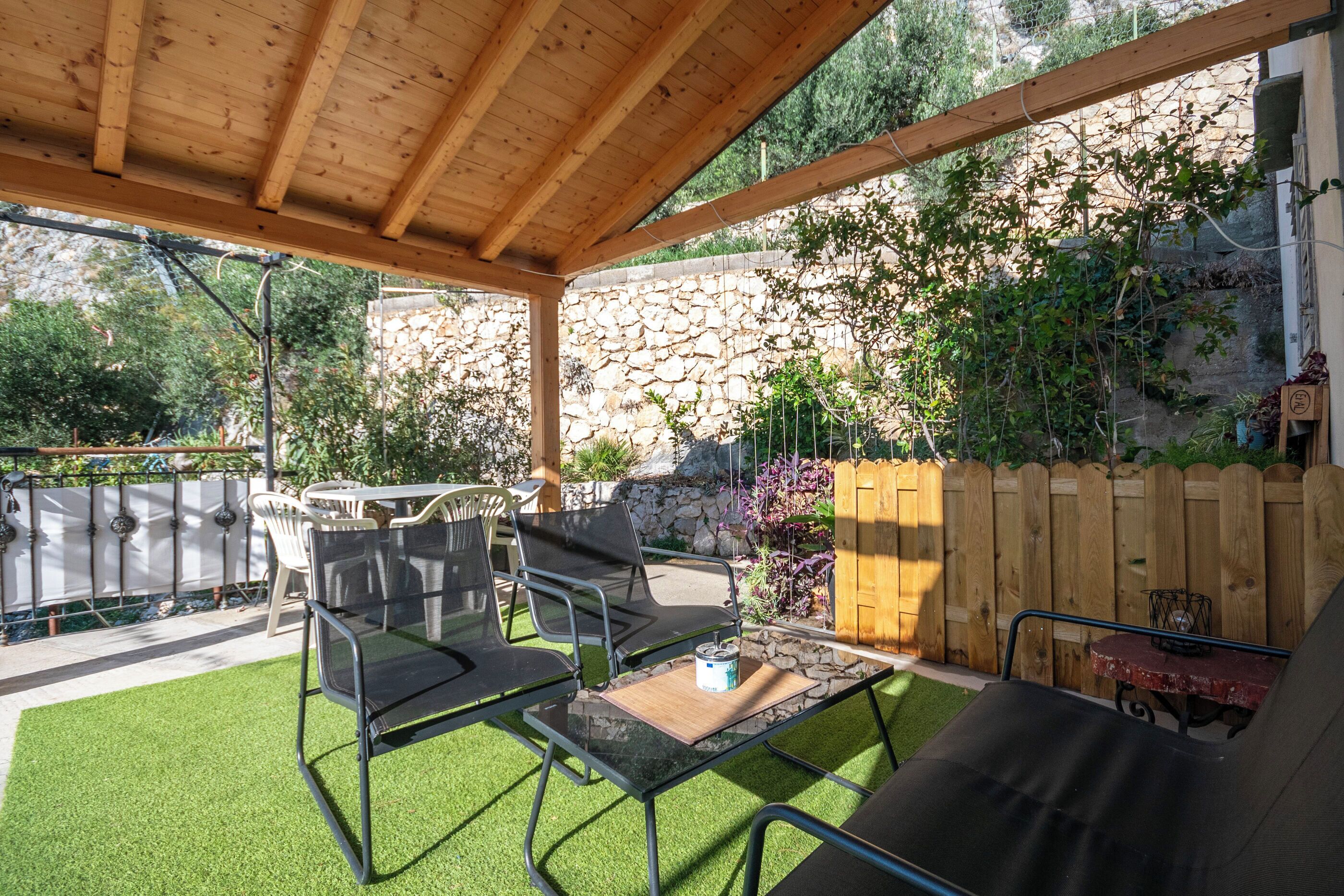 A covered patio with a stone wall, wooden fence, and outdoor furniture.