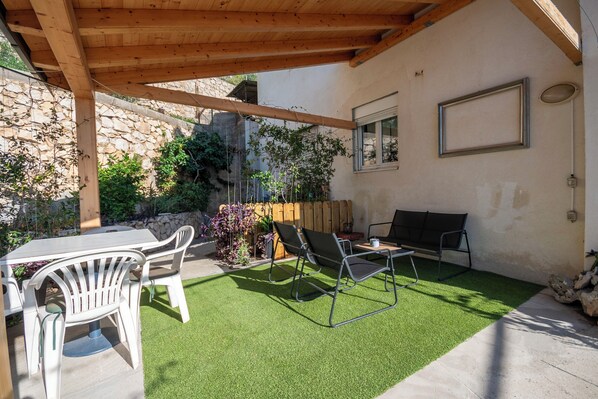 Une terrasse avec une table et des chaises, une pergola en bois et un mur en pierre.