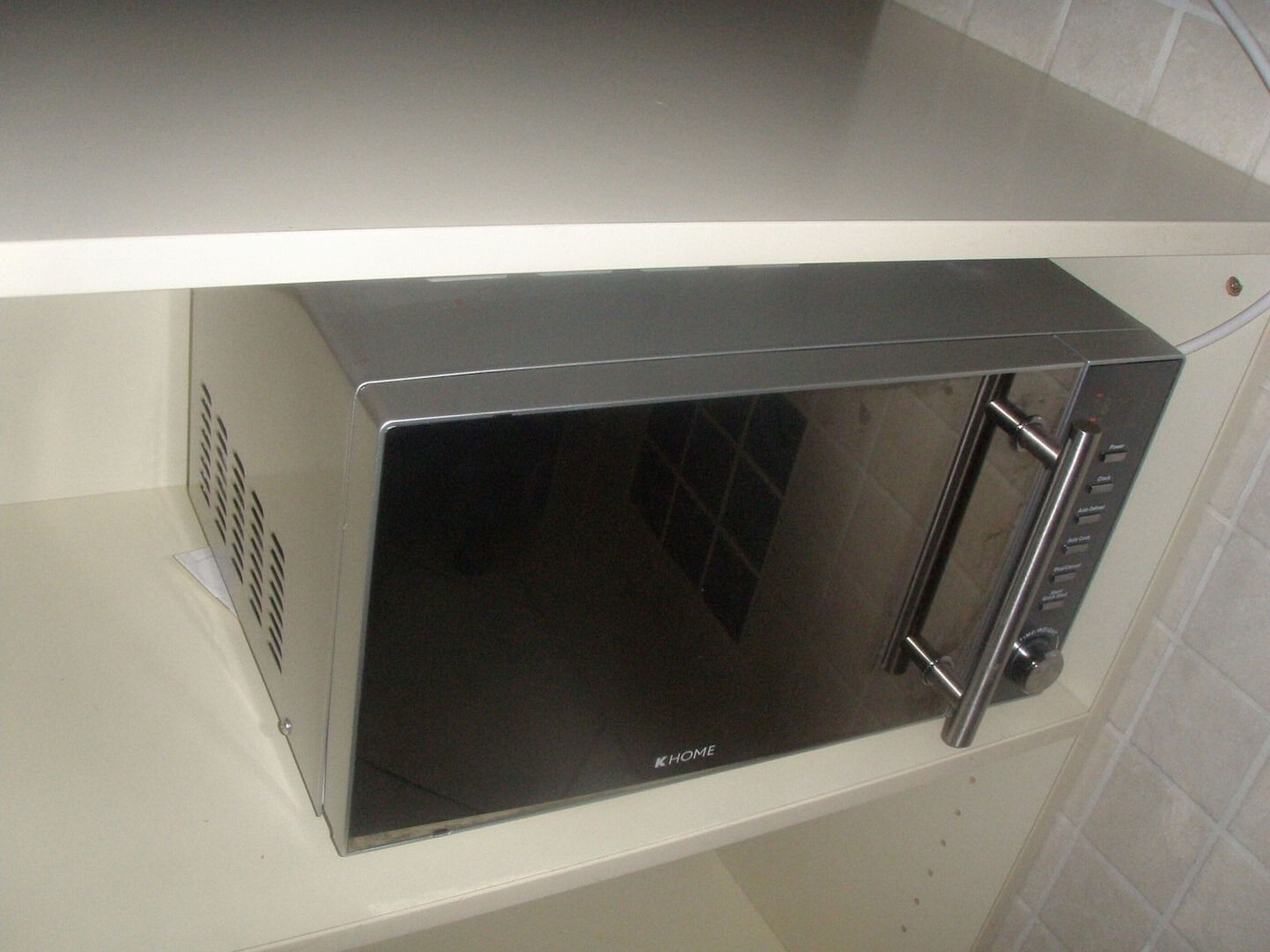 A compact, stainless steel microwave oven with a digital display and control panel, placed on a white countertop.