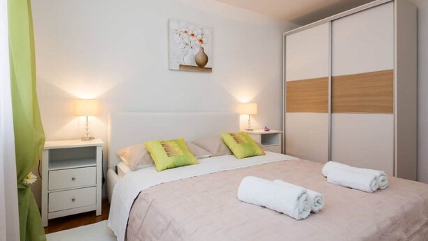 A neatly arranged bedroom with a bed, bedside tables, a wardrobe, and a wall-mounted artwork. - Apartment Dragica 1 (Split)