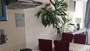 A kitchen with a stove, oven, and blue cabinets. There is a dining table with chairs and a potted plant. - Apartment Dragica 1 (Split)