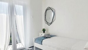 A modern bedroom with a bed, a bedside table, a potted plant, and a large window with sheer curtains. - Apartment Korni (Biograd na Moru)