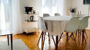 A dining area with a round table, white chairs, a coffee machine, and a shelf with a kettle. - Apartment Korni (Biograd na Moru)