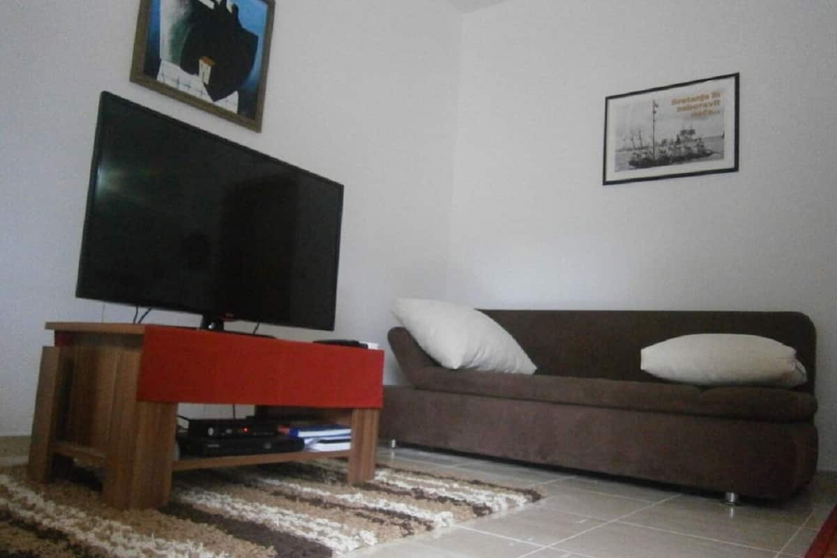 A living room with a flat-screen TV on a wooden stand, a brown sofa with a white cushion, and a framed picture on the wall.