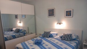 Een slaapkamer met een bed, nachtkastje, spiegel en wanddecoratie.
