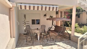 Een terras met een tafel, stoelen, een schommel en een overdekt gedeelte.