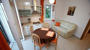 A compact living space with a kitchenette, a dining area with two chairs, a sofa, and a painting on the wall. - Apartments Paula (Sutivan)