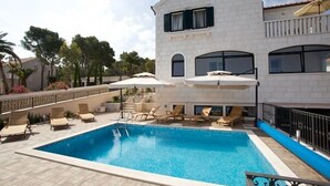 A swimming pool with lounge chairs and umbrellas, surrounded by a white building with a balcony. - Apartments Paula (Sutivan)