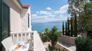 A balcony with a table set for breakfast, overlooking a coastal view with the sea and mountains in the distance. - Apartments Paula (Sutivan)
