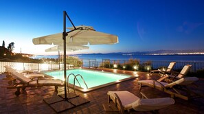 A poolside area with lounge chairs and a pool, overlooking a body of water and distant city lights. - Apartments Paula (Sutivan)