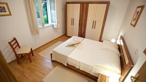 A bedroom with a wooden bed, a chair, a window with curtains, and a bedside lamp. - Apartments Paula (Sutivan)