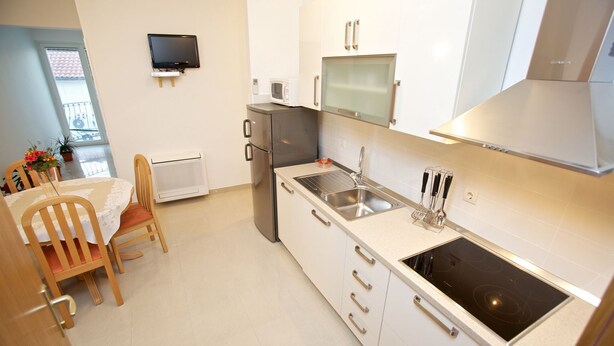 A modern kitchen with a built-in stove, a sink, and a microwave. There is a dining table with chairs and a TV mounted on the wall. - Apartments Paula (Sutivan)