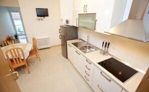 Een moderne keuken met een inbouwfornuis, een spoelbak en een magnetron. Er staat een eettafel met stoelen en een televisie hangt aan de muur.