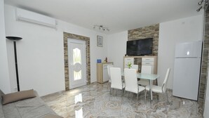 A modern living room with a sofa, a dining area with chairs and a table, a kitchen with a refrigerator, and a TV mounted on the wall. - Apartments Ivica (Kastela)