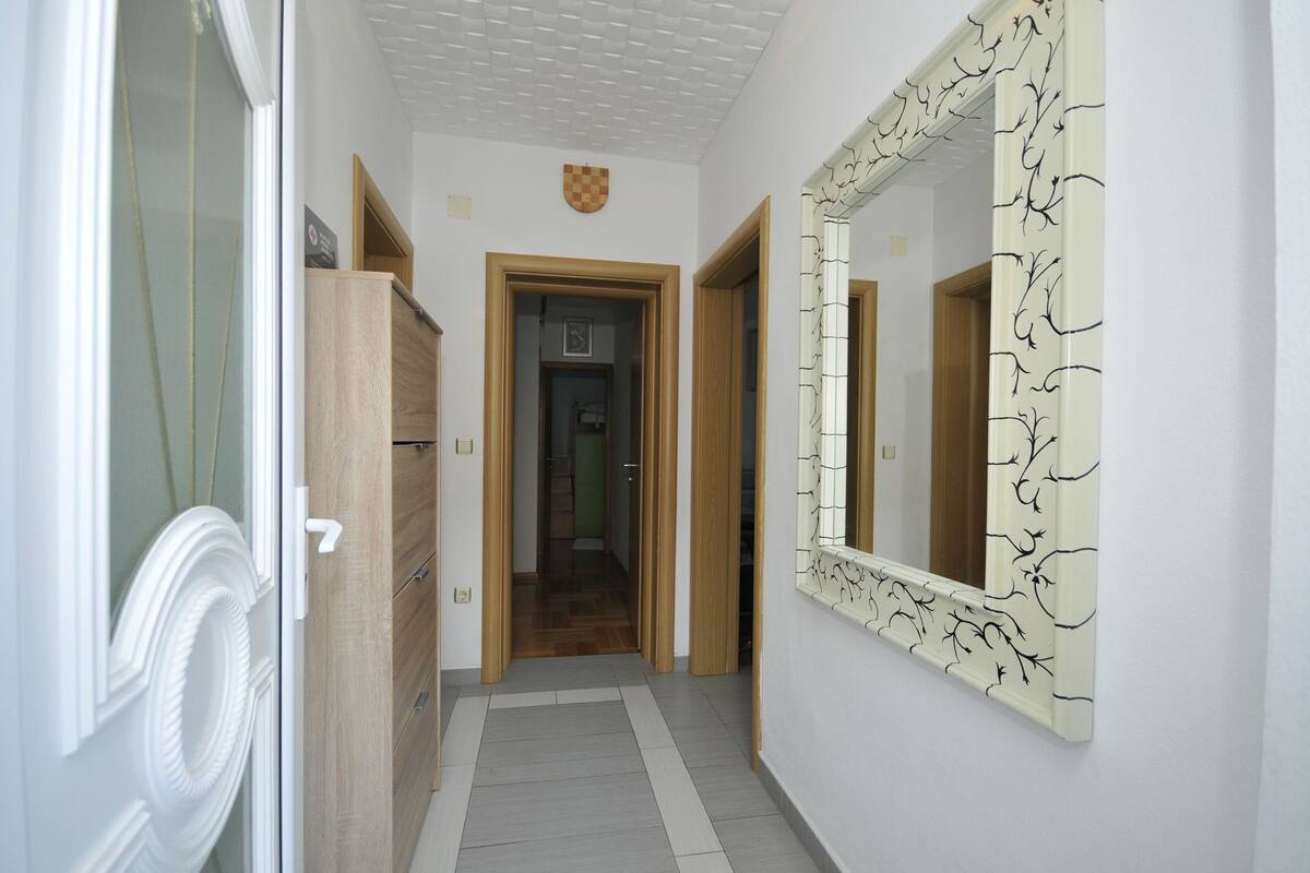 Un couloir avec une armoire en bois, une porte ornée de blasons et un miroir décoré d’un motif d’arbre.