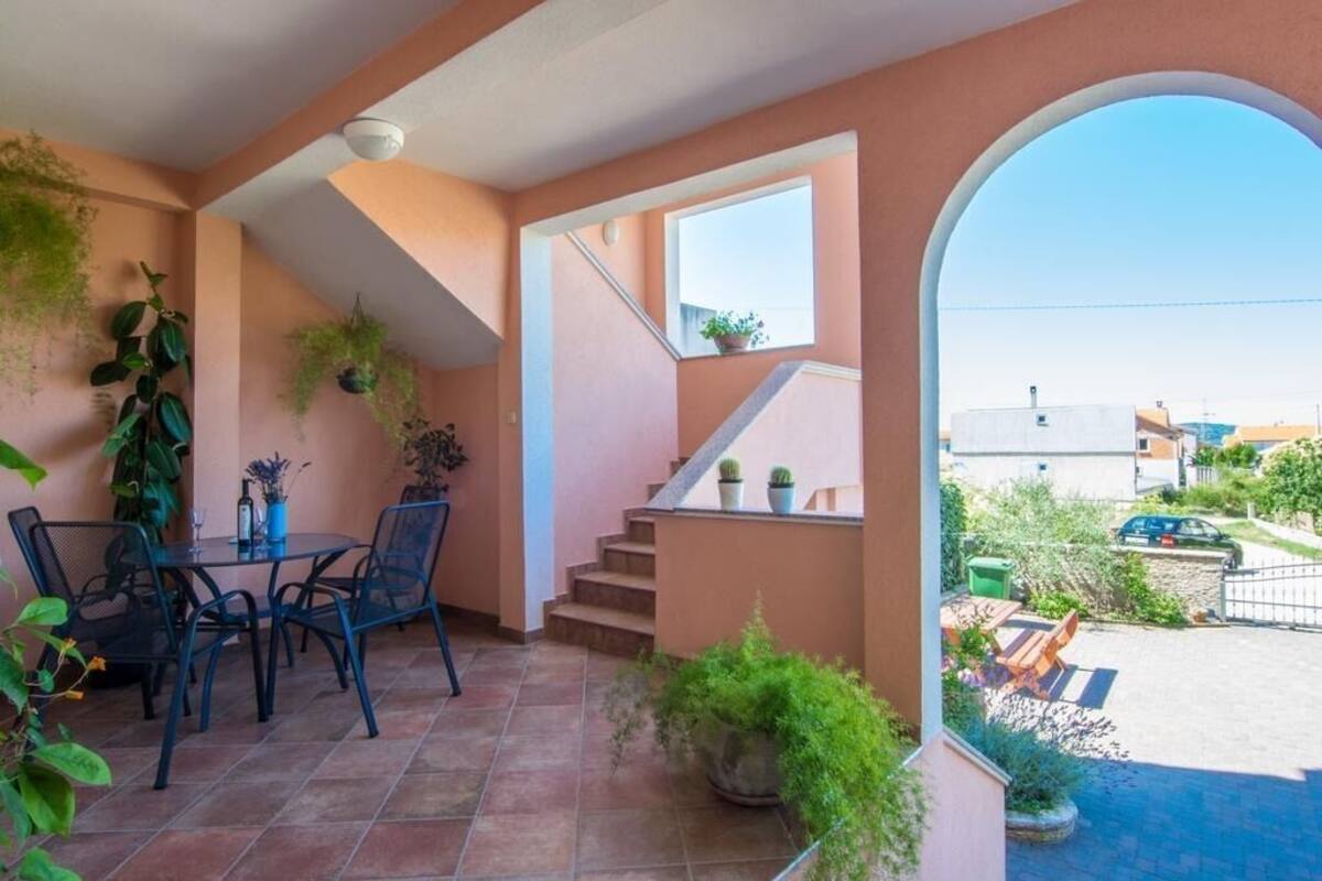 A balcony with a table and chairs, potted plants, and a view of the street.