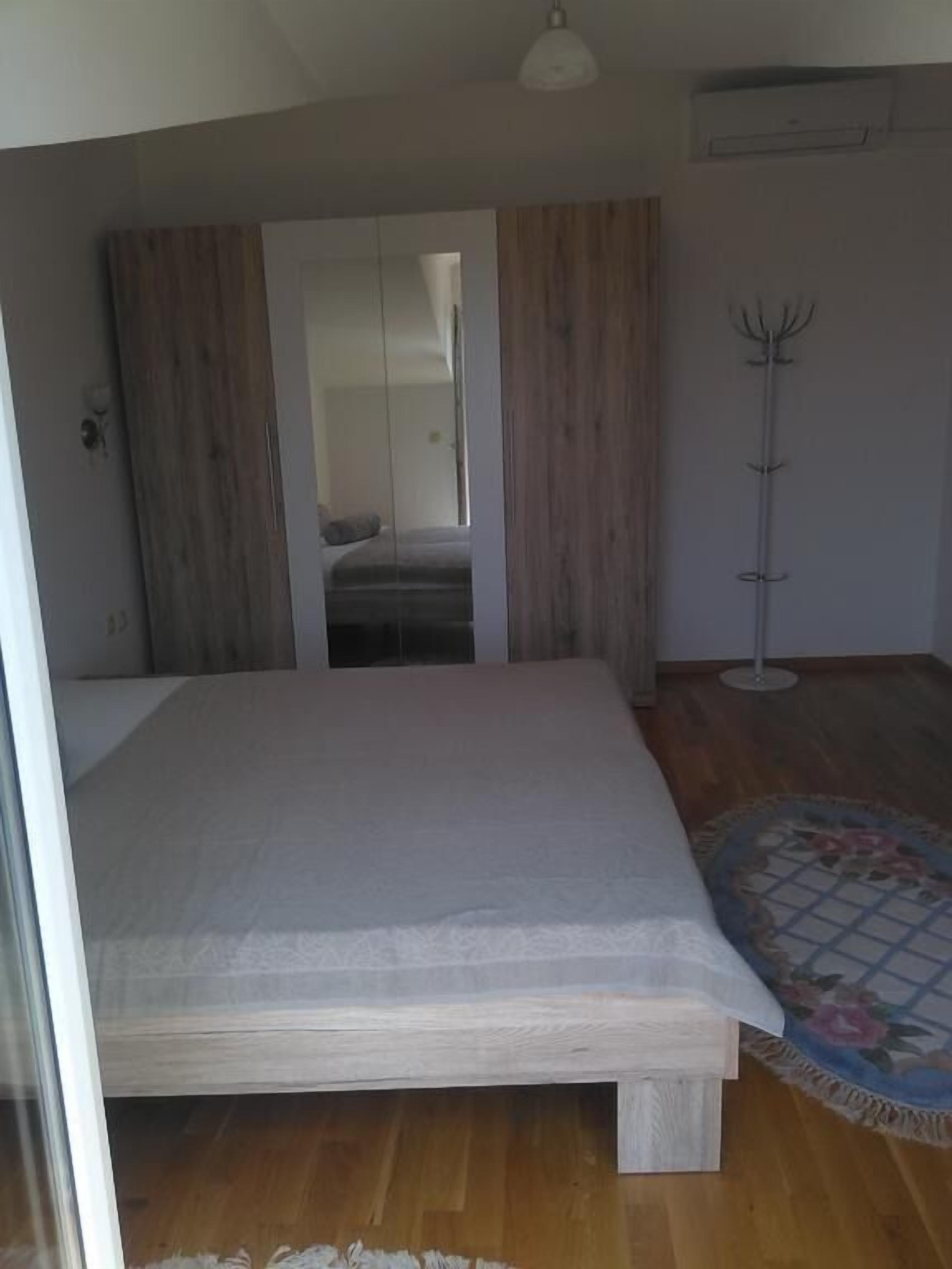 A bedroom with a bed, a wooden floor, a coat rack, and a mirror.