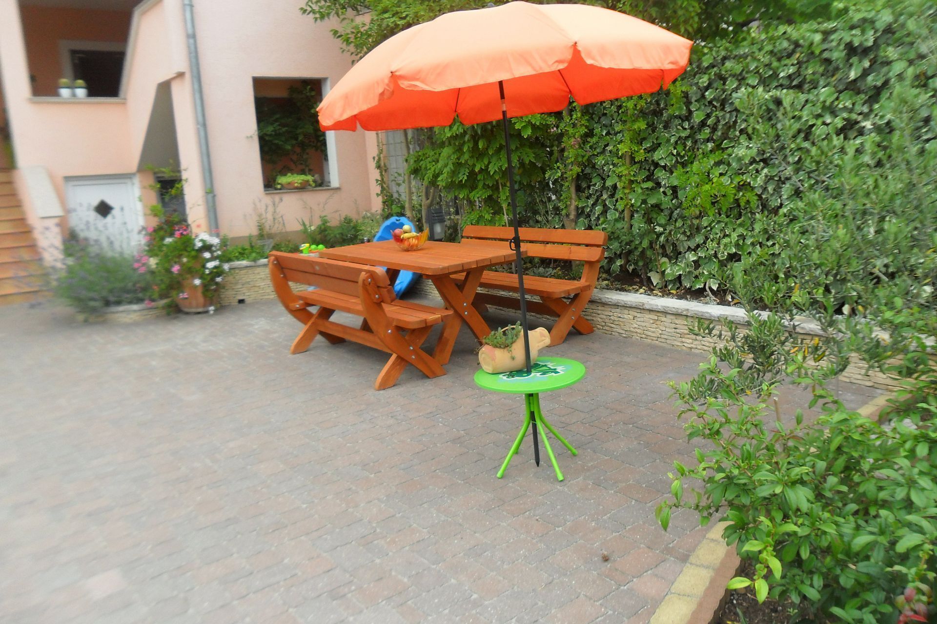 Une terrasse extérieure avec une table et des chaises en bois, une petite table ronde verte et un parasol orange.